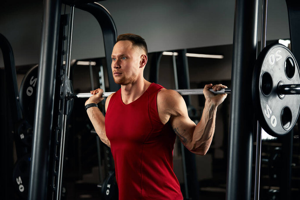 Κοντινό πορτρέτο ενός μυώδους άνδρα προπόνηση με barbell στο γυμναστήριο. Σκληρός bodybuilder αθλητικός άνθρωπος με έξι πακέτο, τέλειο κοιλιακούς, ώμους, δικέφαλους, τρικέφαλους και στήθος - Φωτογραφία, εικόνα