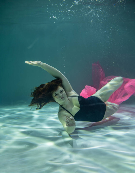 beautiful girl in a black swimsuit and with a pink pareo underwater on a blue background - Foto, immagini