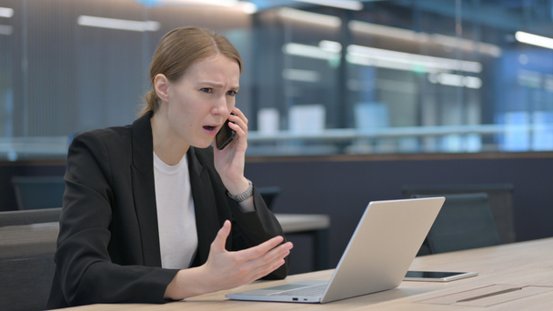 Angry Businesswoman Talking on Smartphone while using Laptop  - Foto, Bild