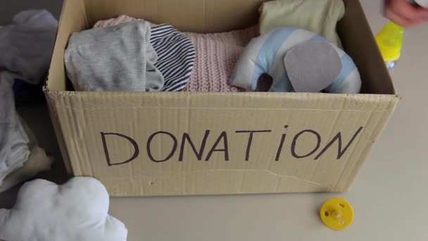 Una mujer pone ropa de bebé y juguetes en una caja de donaciones. Ayudar a los pobres - Imágenes, Vídeo