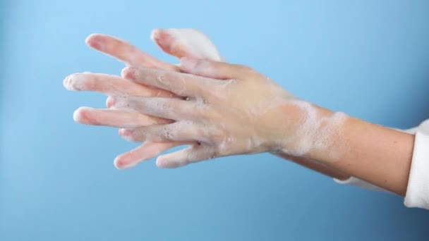 Nainen vaahdottaa ja pesee kätensä sinisellä taustalla lähikuva.  - Materiaali, video