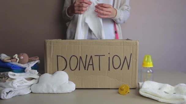 Een vrouw stopt babykleertjes en speelgoed in een donatiekist. De armen helpen - Video