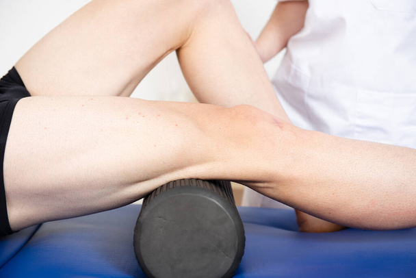 Vista de cerca de un atleta usando un rodillo de espuma en un centro de fisioterapia. - Foto, imagen