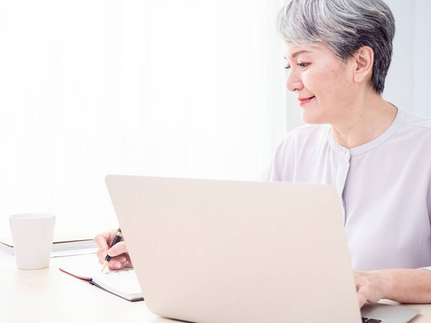 Moderna anciana de pelo gris de 60 años mujer tomar curso en línea o formación en el ordenador en casa. - Foto, imagen