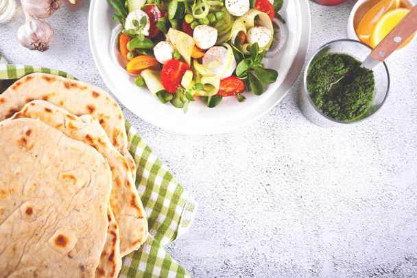 salad of fresh cherry tomatoes, mozzarella, basil and other greens on the dinner table with pita flat bread - Φωτογραφία, εικόνα