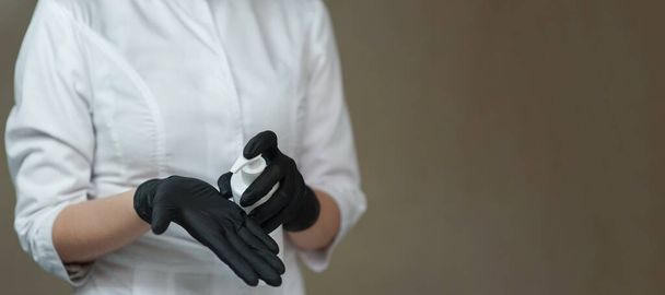 médico esteticista aperta anti-séptico de um frasco branco com um dispensador em luvas médicas pretas - Foto, Imagem