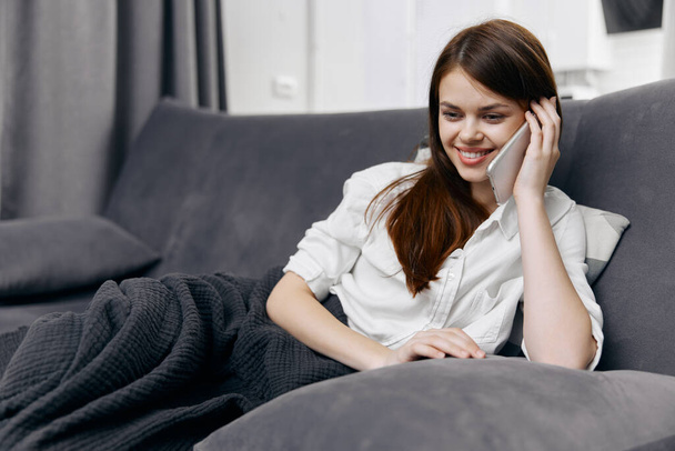 onnellinen nainen puhuu puhelimessa sohvalla sisätiloissa - Valokuva, kuva