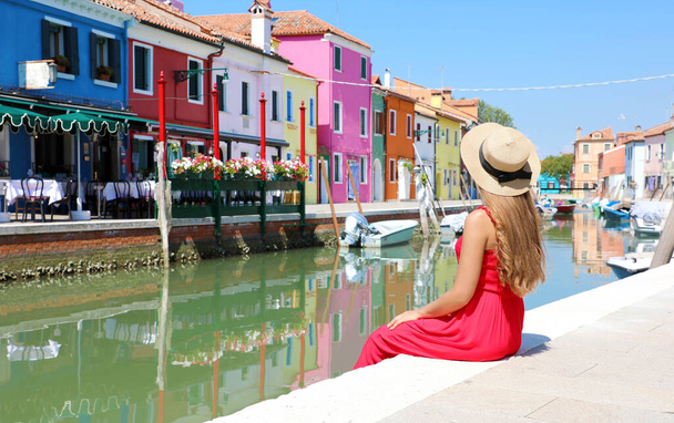 Turismo en Venecia. Vista panorámica de la bandera de la mujer bonita en vestido rojo sentado y mirando el viejo pueblo colorido de Burano en Venecia, Italia. - Foto, imagen