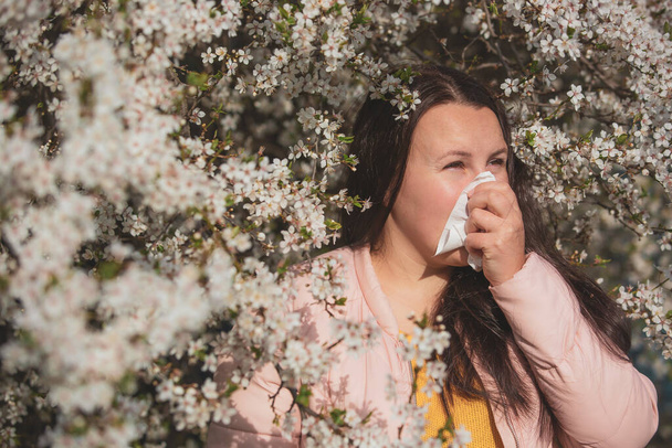 Concetto di sintomi allergici primaverili, giovane donna che starnutisce di fronte alla fioritura di un albero, allergia al polline e alla stagione della fioritura, sanità - Foto, immagini