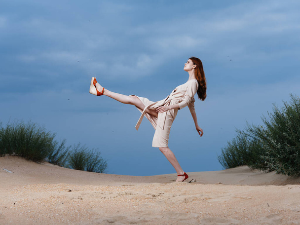 ベージュのドレスを着た女性がビーチを歩いている - 写真・画像