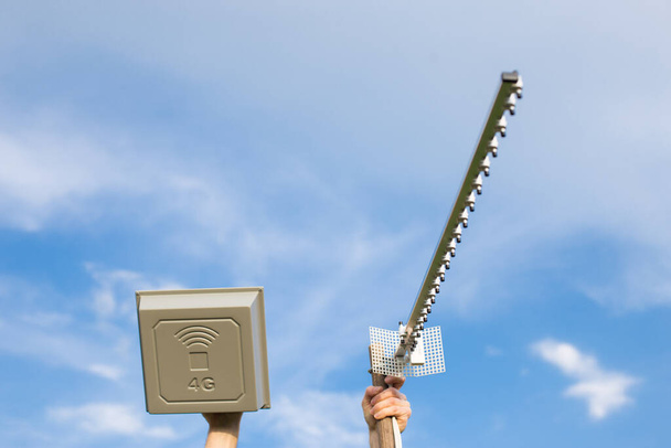 Handen met twee verschillende antennes voor mobiel internet 4G en 5G, om de dekking te verbeteren, met blauwe lucht achtergrond. - Foto, afbeelding