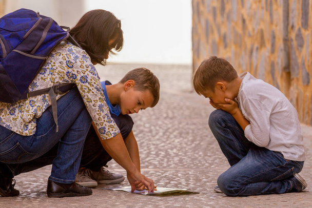 Moeder met twee kinderen op zoek naar papieren kaart om bestemming te vinden in de oude Europese stad straat - Foto, afbeelding