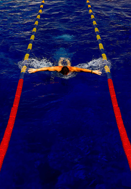 un atleta nada pecho en una piscina al aire libre, un hombre hace deportes en el agua, el agua azul de un estanque artificial con la gente - Foto, Imagen