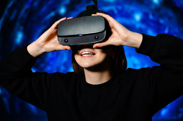 Chica feliz utiliza gafas de realidad virtual sobre fondo azul de la sala de juegos. Foto de alta calidad - Foto, Imagen