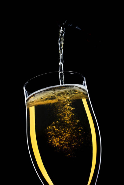 una cerveza vertiendo en un vaso sobre un fondo negro - Foto, imagen