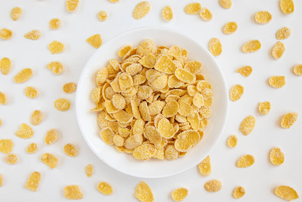 cornflake in schaal op witte achtergrond, bord cornflakes, gezond ontbijtconcept, cornflakes verkruimeld rond de beker, bovenaanzicht - Foto, afbeelding