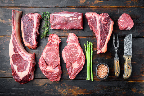 Variété de steaks de viande crus Black Angus Prime, tomahawk, t os, steak club, côtes levées et filet, sur un vieux fond de table en bois foncé, vue sur le dessus plat - Photo, image