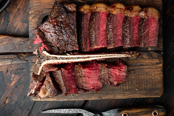 Morceaux de délicieux steak de bœuf moyen et rare, coupé en os ou en porterhouse, sur une planche de service en bois, sur un vieux fond de table en bois foncé, vue sur le dessus plat - Photo, image