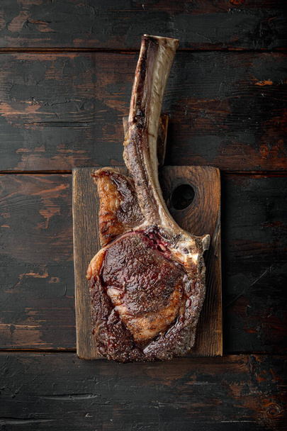 schön gebratenes Tomahawk-Steak, mittelseltenes Set, auf hölzernem Servierbrett, auf altem dunklem Holztischhintergrund, von oben flach liegend - Foto, Bild