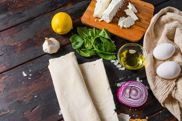 Greek spanakopita ingredients filo spinach eggs feta top view on dark wooden background space for text - 写真・画像