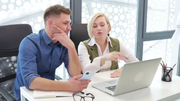 Dva kolegové businesspersons muž a žena spolupracovníci sedí u stolu v moderní kanceláři při pohledu na notebook diskutovat o rozpočtu práce mužské pojištění agent pomáhá dívce s financemi konzultace pomocí počítače - Záběry, video