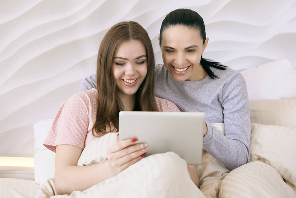 Mother with her teenage daughter watching movie on tablet pc screen in bed. - Photo, Image