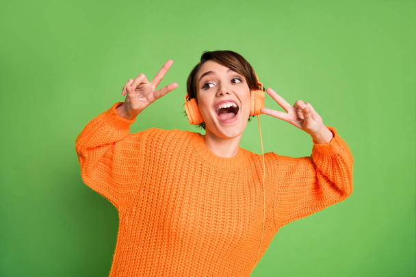 Photo of excited happy young woman wear headset show two v-signs look empty space isolated on green color background - Valokuva, kuva