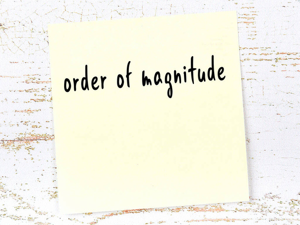 Concept of reminder about order of magnitude. Yellow sticky sheet of paper on wooden wall with inscription - Photo, Image