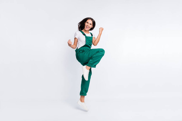 Photo of cheerful astonished lady raise fists open mouth wear green overall sneakers isolated white color background - Valokuva, kuva