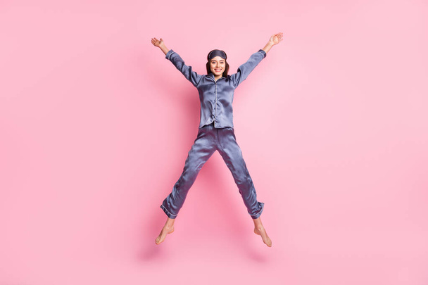 Full length body size photo of girl wearing blue nightwear jumping playful like star smiling isolated on pastel pink color background - Foto, afbeelding