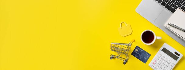 Online shopping concept. Top view of credit card purchase design concept with note, calculator and computer isolated on office yellow table background. - 写真・画像