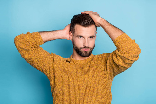 Photo of young confident serious handsome cool man fixing hairstyle wear yellow knitted sweater isolated on blue color background - Fotoğraf, Görsel