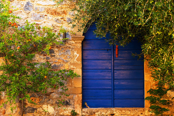 A house with a closed blue door and a pomegranate tree in front of him in the medieval tourist town of Monemvasia, Peloponnese, Greece - Фото, изображение