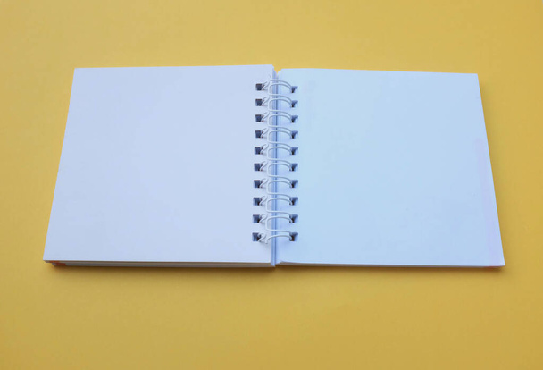  Pusty pusty pusty biały notatnik spiralny izolować na żółtym tle.Wyposażenie biurowe lub edukacyjne. - Zdjęcie, obraz