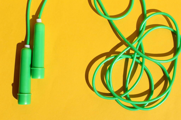 Green fitness jump rope lies on a yellow background - Фото, зображення