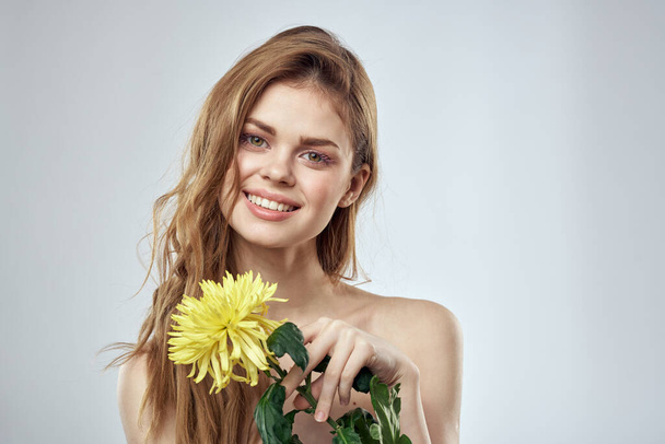 Portret van een mooie vrouw met een gele bloem op een lichte achtergrond bijgesneden met Copy Space Model - Foto, afbeelding