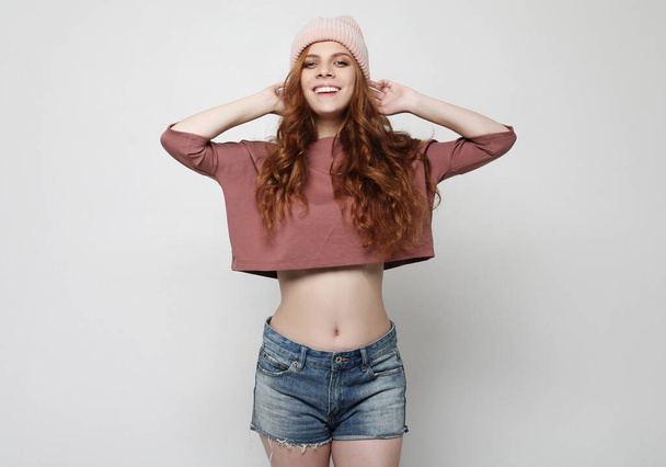 Beautiful young happy woman wearing pink hat and denim shorts over grey background - 写真・画像