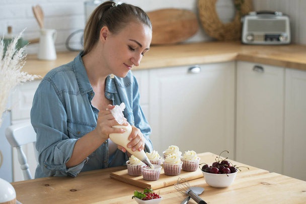 Young Woman making creamy top of cupcakes closeup. - 写真・画像