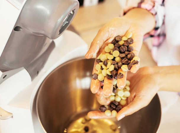 Primo piano mani femminili che tengono gocce di cioccolato - bianco e marrone, per fare ganache al cioccolato - Foto, immagini