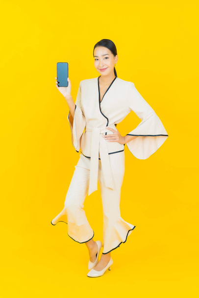 Ritratto bella giovane impresa donna asiatica con smart cellulare su sfondo giallo - Foto, immagini