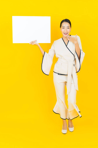 Portrait beautiful young business asian woman with empty white billboard card on yellow background - Photo, Image