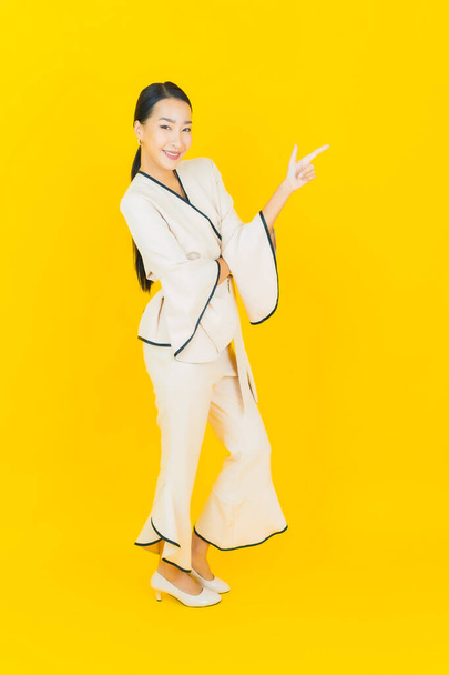 Portret mooie jonge business aziatische vrouw met glimlach en actie gele achtergrond - Foto, afbeelding