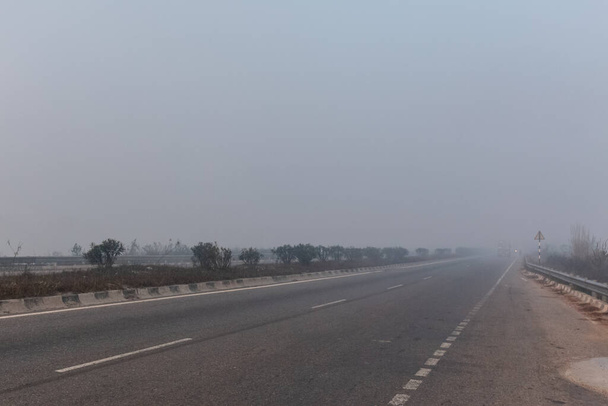 BAREILLY, UTTAR PRADESH, INDIA - DECEMBER 2020: Indian Road Highways, Beautiful landscape of Indian roads during köd and sunrise in winter morning. Autópályán közlekedő járművek. - Fotó, kép