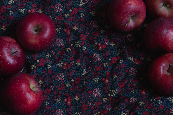 Red apples on a dark fabric in a red floral pattern. Copy space. - Zdjęcie, obraz