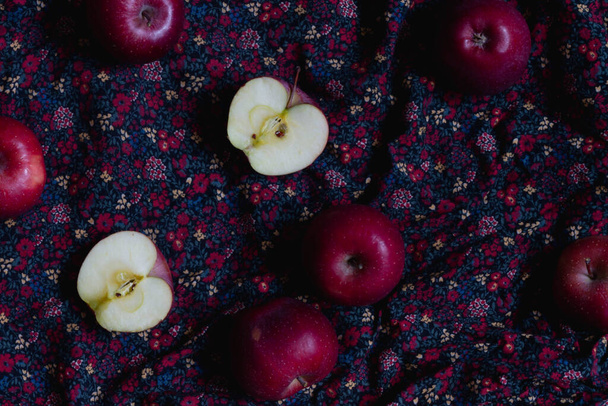 a few red apples on a fabric with a floral pattern. whole and cut fruit apples. - Foto, Imagen