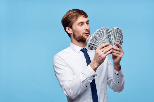 πλούσιος άνδρας με κοστούμι με χρήματα στα χέρια συναισθήματα μπλε φόντο - Φωτογραφία, εικόνα