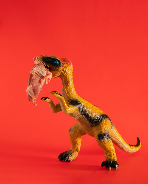 Kırmızı arka planda ağzında taze et olan dinozor oyuncağı. Soyut sanat. asgari yaratıcı soyut sanat - Fotoğraf, Görsel