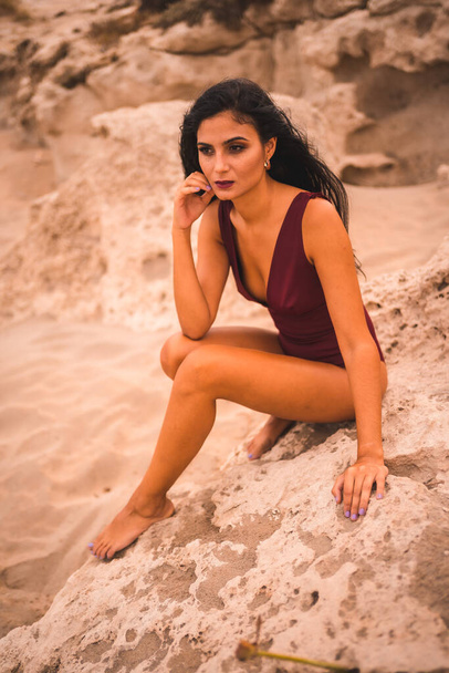 Caucasian brunette in a maroon swimsuit, sitting smiling on the beach of Cabo de Gata, Nijar. Andalucia, Spain - Foto, afbeelding