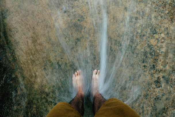 Pie de hombre de pie sobre una roca en una cascada - Foto, Imagen