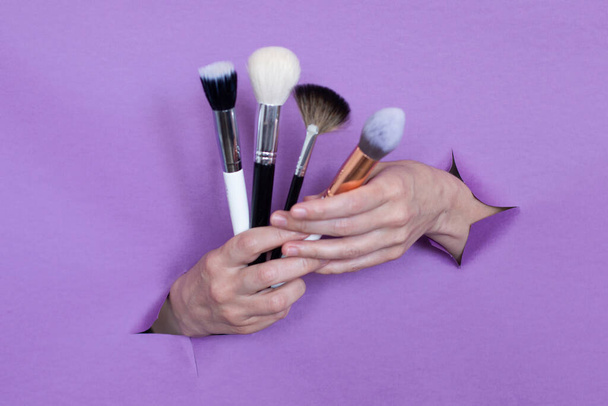 profesionální make-up štětce v rukou, na fialovém pozadí, díry v pozadí. Mezera pro text. - Fotografie, Obrázek
